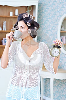 Beautiful woman in hair curlers drinking coffee in the morning