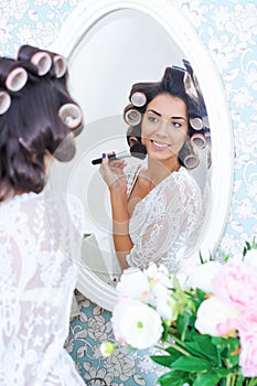 Beautiful woman in hair curlers puts on morning makeup