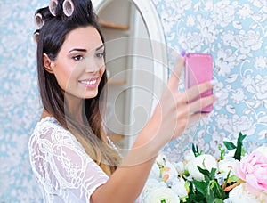 Beautiful woman in hair curlers taking selfie photo