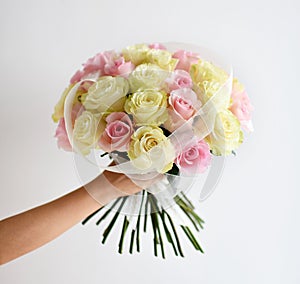 Beautiful woman hand hold bouquet of yellow and pink roses flowers on white