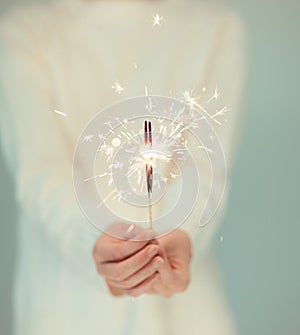 Beautiful woman hands holding sparkler lights, cozy, bright winter sweater,