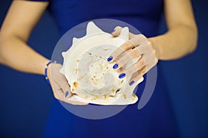 Beautiful woman hands with perfect nail polish holding big sea snail shell in front of blue dress