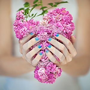 Beautiful woman hands with perfect violet pink and turquoise nail polish holding pink roses