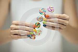 Beautiful woman hands with rainbow nail polish holding colorful swirl lollypops, funny cheerful