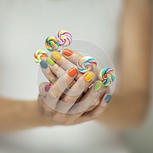 Beautiful woman hands with rainbow nail polish holding colorful swirl lollypops, funny cheerful