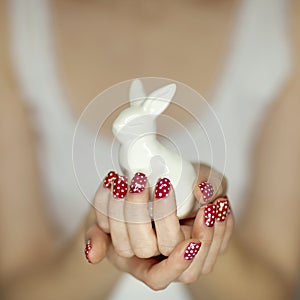 Beautiful woman hands with red nail polish art holding easter bunny