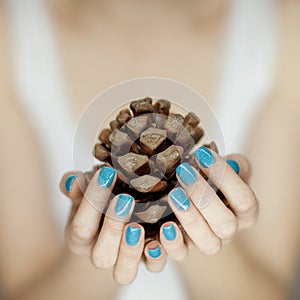 Beautiful woman hands with turquoise nail polish art holding fir cone