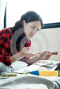 A beautiful woman has lain down on the bed at a condominium and shopping online on a laptop by the credit card with unhappy and