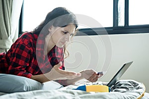 A beautiful woman has lain down on the bed at a condominium and shopping online on a laptop by the credit card with unhappy and