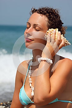 Beautiful woman has leant seashell bowl to an ear