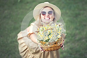 Beautiful woman in hat and with a basket of field daisies in sunny summer day.