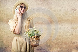 Beautiful woman in hat and with a basket of field daisies talking on a cell phone.