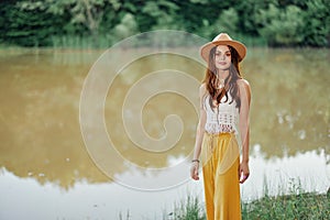 Beautiful woman in a hat and eco-dress hippie look outdoors by the lake walking