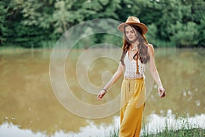 Beautiful woman in a hat and eco-dress hippie look outdoors by the lake walking