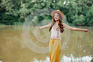 Beautiful woman in a hat and eco-dress hippie look outdoors by the lake walking