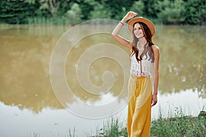 Beautiful woman in a hat and eco-dress hippie look outdoors by the lake walking