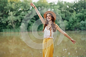 Beautiful woman in a hat and eco-dress hippie look outdoors by the lake walking