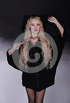 Beautiful woman in hat with magic wand on dark background.