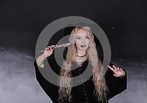 Beautiful woman in hat with magic wand on dark background.