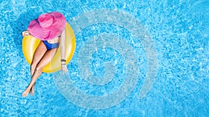 Beautiful woman in hat in swimming pool aerial view from above, young girl in bikini relaxes and swims on inflatable ring donut