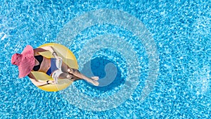 Beautiful woman in hat in swimming pool aerial view from above, young girl in bikini relaxes and swims on inflatable ring donut