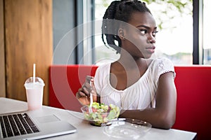 Beautiful woman have lanch eat salad at dinner sitting at cafe. Young african american woman sitting in a coffee shop and working