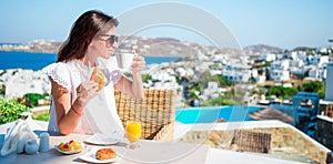 Beautiful woman having breakfast at outdoor cafe with amazing view. Girl enjoy her hot coffee early in the morning