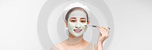 Beautiful woman having clay facial mask apply by beautician