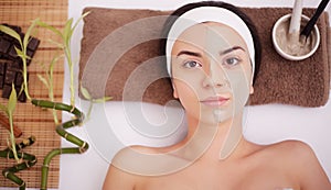 Beautiful woman having clay facial mask apply by beautician.