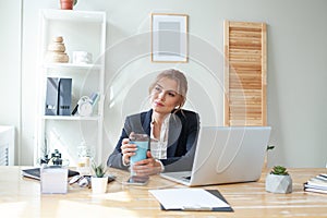 Beautiful woman having coffee at her desk in the office. Young woman drinking coffee at the workplace