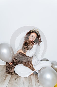 A beautiful woman having fun with her Spanish water dog in a New Year`s Eve. She is hugging her dog surrounded by balloons while