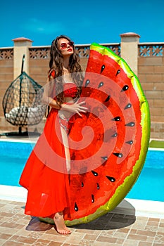 Beautiful woman having fun with watermelon float mattress by swimming pool on villa resort. Sexy girl enjoy summer vacation.