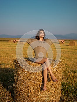 Beautiful woman on hay stack hands wind