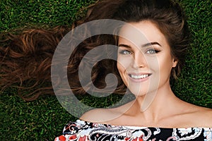 Beautiful woman with a healthy curly hair is lying on the grass