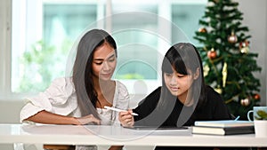 A beautiful woman helping her daughter doing homework online on digital tablet at home.