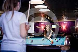 Beautiful woman with her friend playing billiard in pub