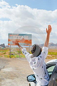 Beautiful woman on her trip by the car. Welcome to Utah road sign. Large welcome sign greets travels in Monument Valley