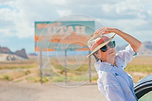 Beautiful woman on her trip by the car. Welcome to Utah road sign. Large welcome sign greets travels in Monument Valley