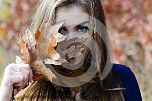 Beautiful woman hiding face behind autumn brown leaf