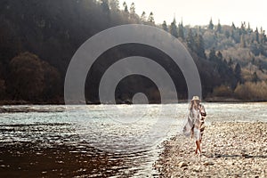 beautiful woman hipster walking on river beach in mountains,wearing hat and poncho, boho travel concept, space for text