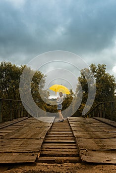 Beautiful woman hold yellow umbrella and walking on a old bridge in the countryside under rain