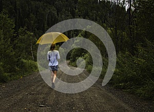 Beautiful woman hold yellow umbrella and walks on a country road under rain