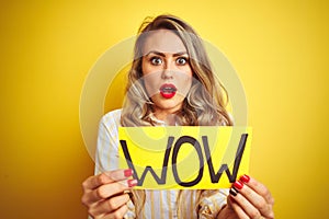 Beautiful woman holding amazed wow surprise banner over isolated yellow background scared in shock with a surprise face, afraid