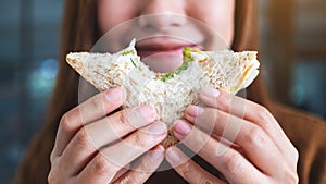 A beautiful woman holding and biting a piece of whole wheat sandwich