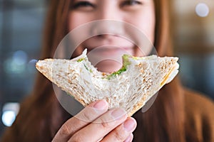 A beautiful woman holding and biting a piece of whole wheat sandwich