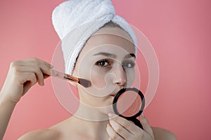 Beautiful woman holding blush brush to apply blush on cheeks on pink background