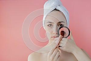 Beautiful woman holding blush brush to apply blush on cheeks on pink background. Copy space