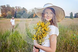 Beautiful woman holding bouquet of yellow flowers and looking at camera with her boyfriend on background.