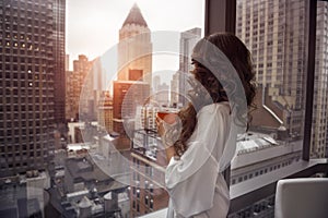 Beautiful woman holding coffee cup and looking to the window in luxury Manhattan penthouse apartments