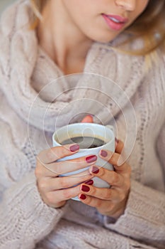 Beautiful woman holding a cup of coffee in her hands. in a knitted beige sweater